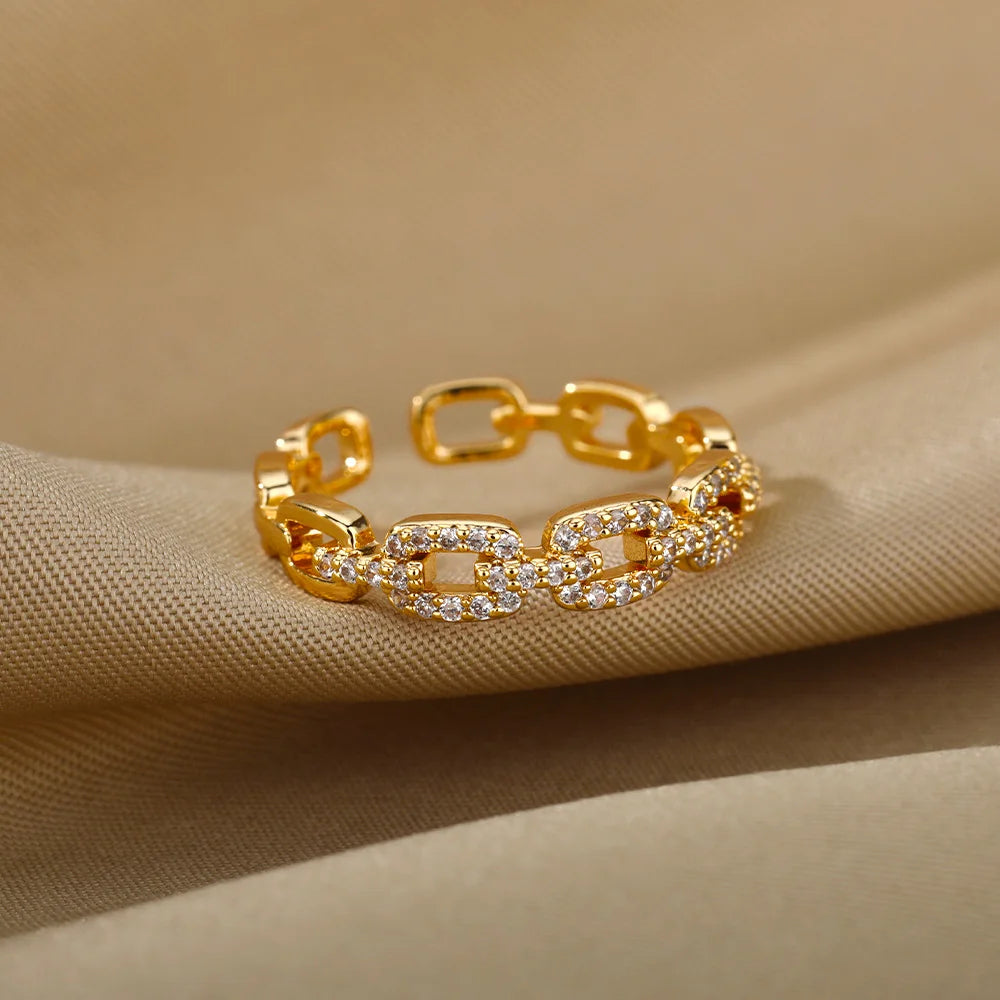 Classic Zircon Twist Chain Rings em ouro com detalhes em zircão brilhante sobre fundo de tecido bege.