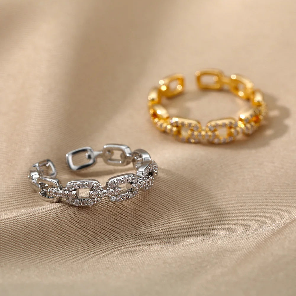 Classic Zircon Twist Chain Rings em ouro com detalhes em zircão brilhante sobre fundo de tecido bege.