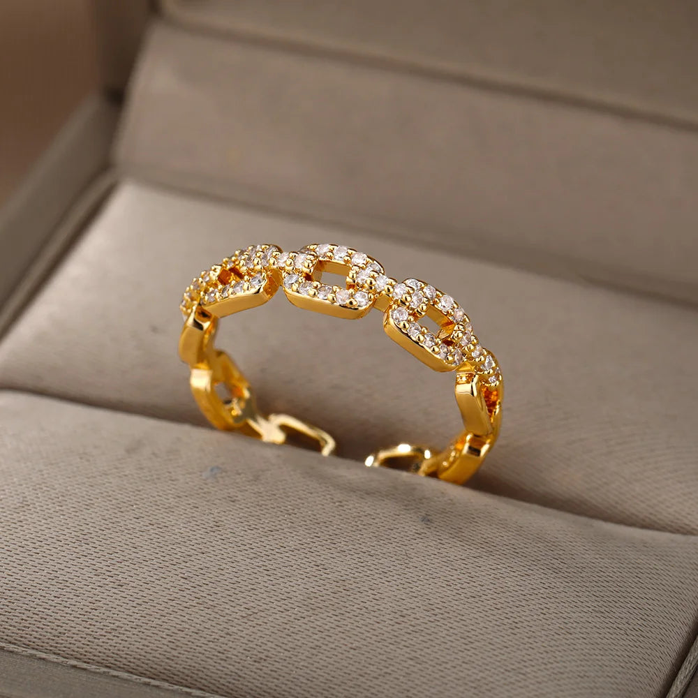 Classic Zircon Twist Chain Rings em ouro com detalhes em zircão brilhante sobre fundo de tecido bege.