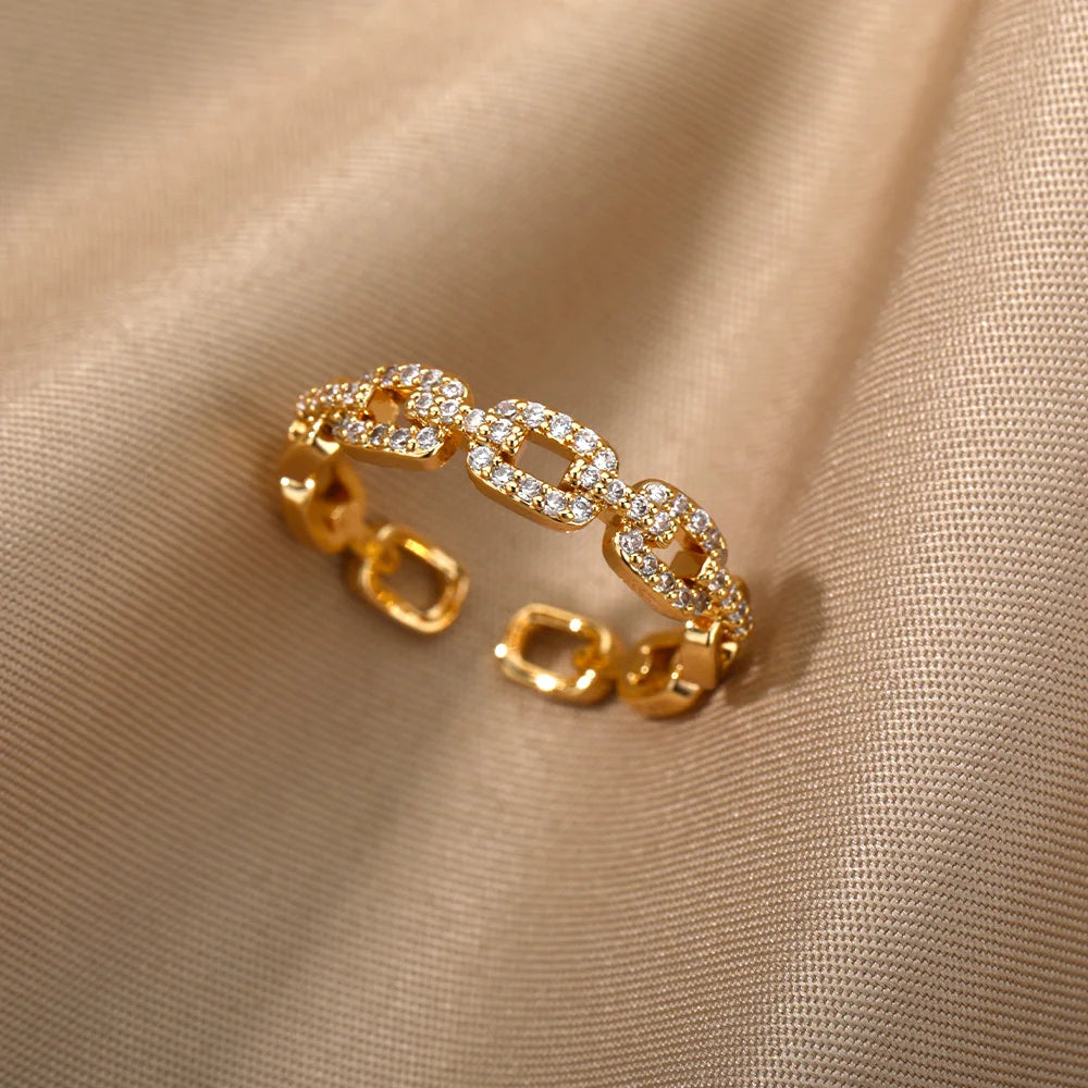 Classic Zircon Twist Chain Rings em ouro com detalhes em zircão brilhante sobre fundo de tecido bege.